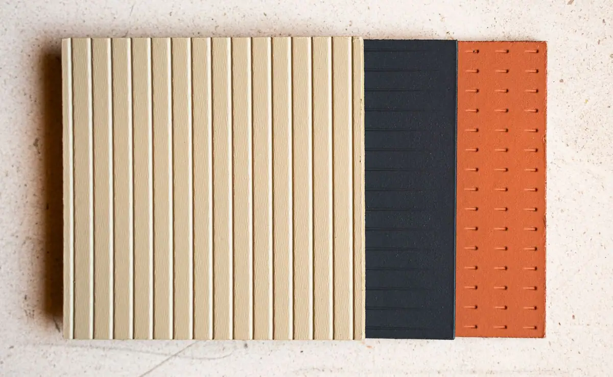 Muestras de panel en tono arena con líneas verticales, gris oscuro con líneas horizontales y terracota con pequeñas marcas