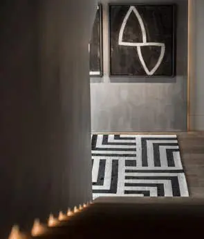 Recibidor con pared de tono cálido, cuadro abstracto en blanco y negro y alfombra de motivos geométricos.