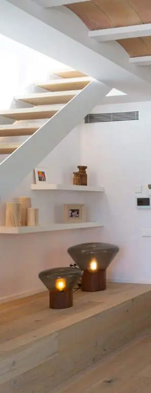 Escalera blanca de peldaños de madera volados sobre un banco corrido de madera con dos lámparas de sobremesa.