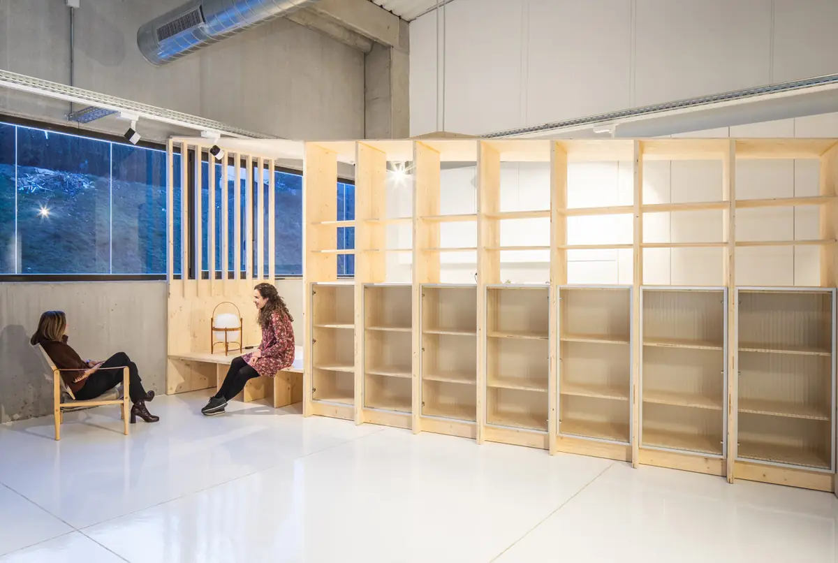 Pale wood shelving unit with a break-out nook in an industrial building with white walls
