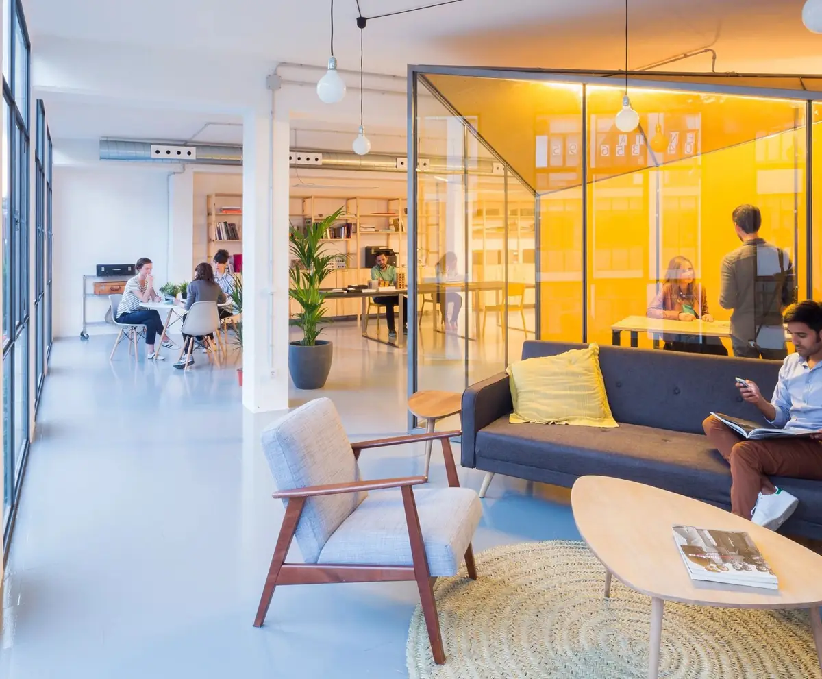 Bright office with a blue sofa, an armchair and a glazed room with a yellow interior in the background