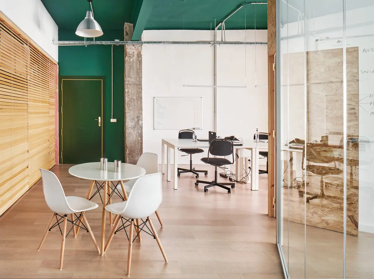 Office with a green ceiling, a round white table and a glass module on the right