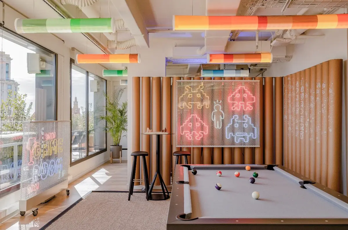 Room with a pool table, space-invader neon signs on the wall and coloured tubes on the ceiling