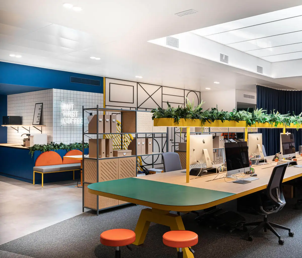 Office with a green table and orange stools, workstations with computers and a raised planter