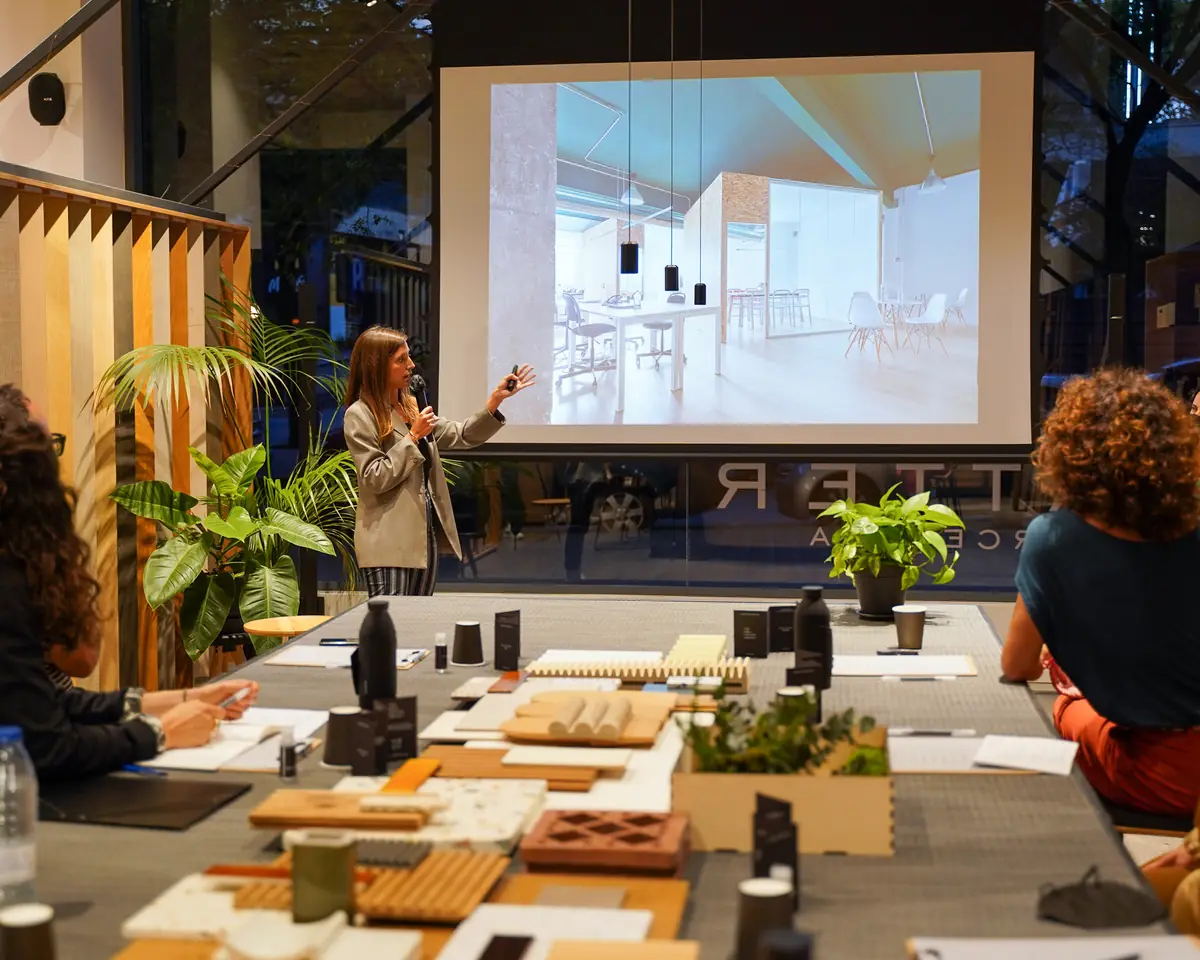 A speaker presenting an office project on screen in front of the materials table