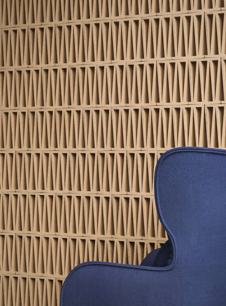 Wall of Celosia terracotta pieces with a repeated triangular motif behind a blue armchair