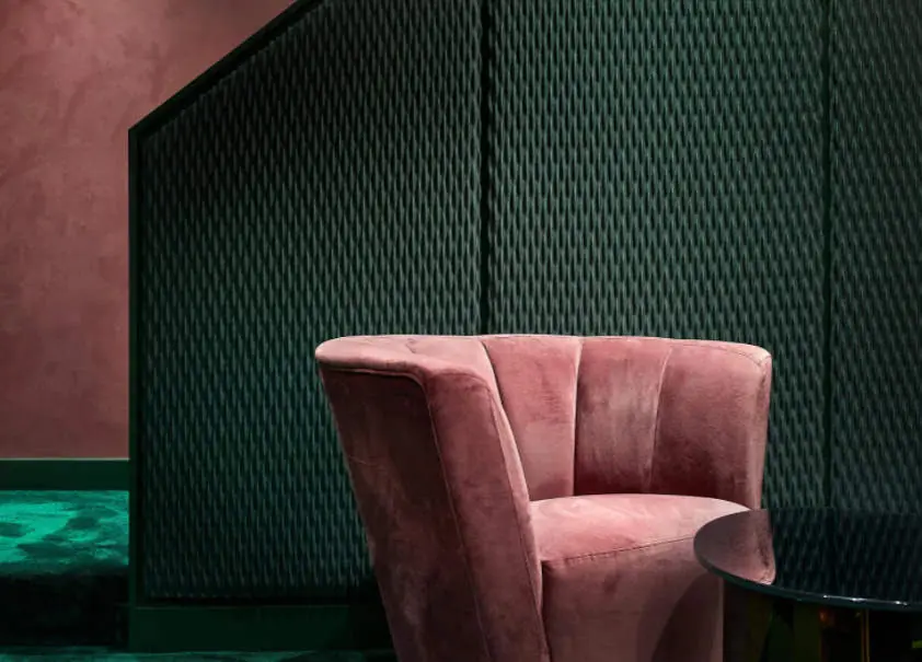 Pink velvet armchair in front of a wall clad with green textured textile panels