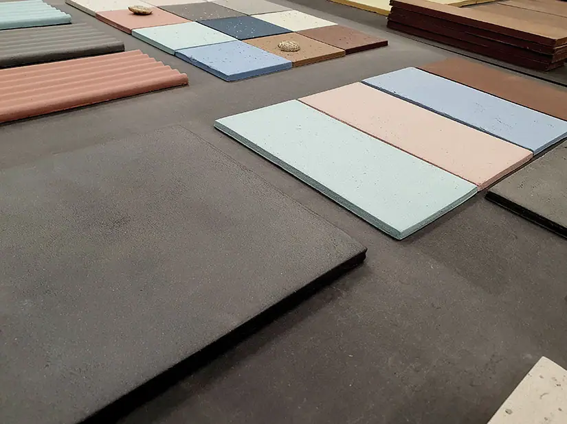 Baldosas de gres de varios colores y formatos sobre una mesa, con piezas onduladas al fondo