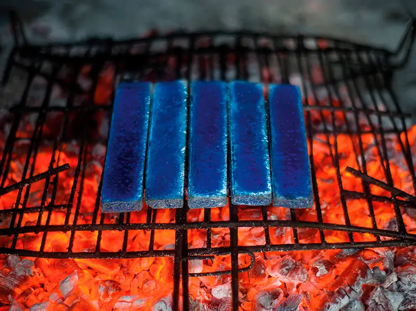 Cinco azulejos rectangulares esmaltados en azul sobre una parrilla con brasas