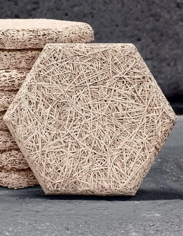 Baldosa acústica hexagonal de lana de madera en tono natural apoyada junto a una pila de baldosas