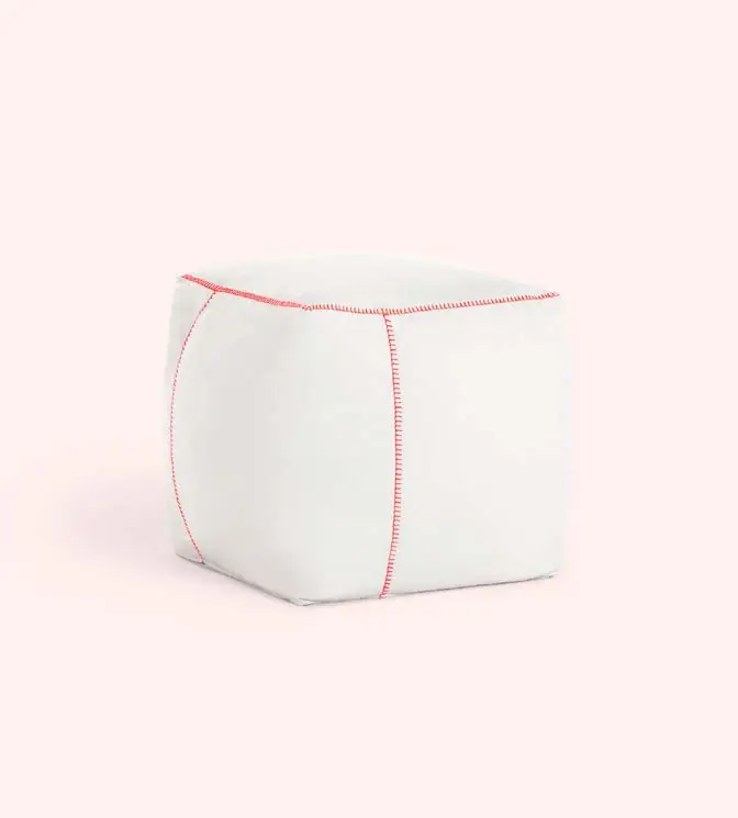 White cube-shaped pouf with contrasting red seams against a light pink background