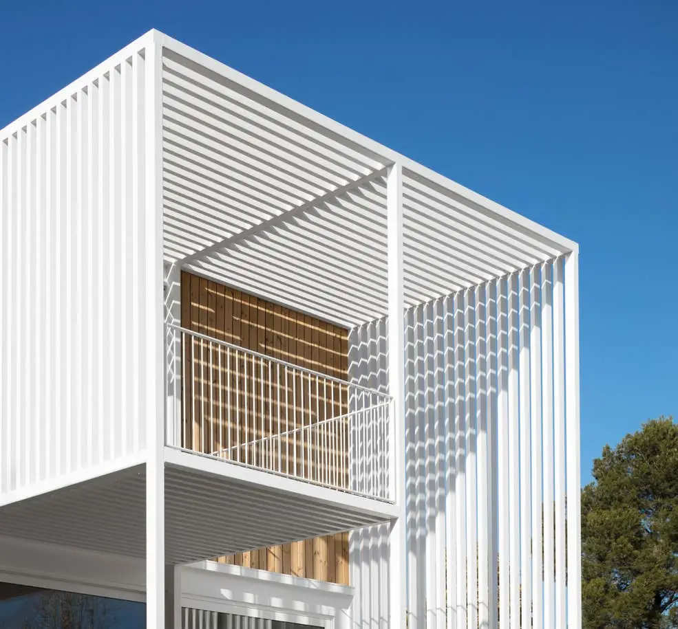 Casa con una piel exterior de lamas metálicas blancas que envuelve un volumen interior de madera