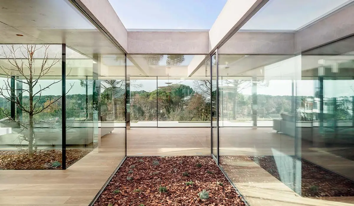 Patio interior con árboles rodeado de paños de vidrio que reflejan el exterior