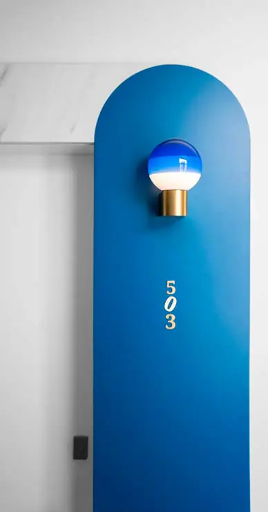 Puerta azul en arco con número de habitación y aplique de luz