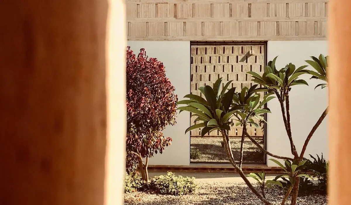 Brick lattice behind a garden with palm trees, framed by an earth-toned wall