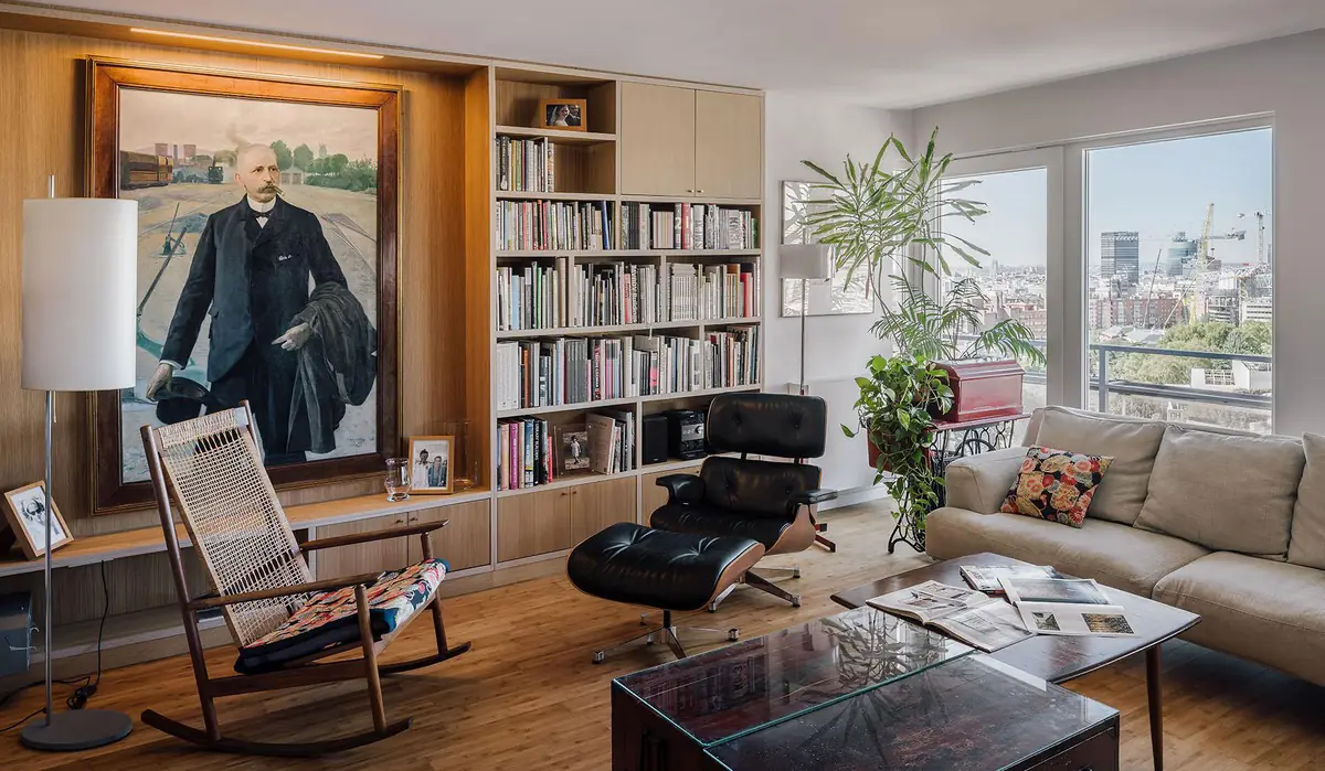 Living room with bespoke wooden bookcase, black leather armchair, rocking chair and large windows over the city