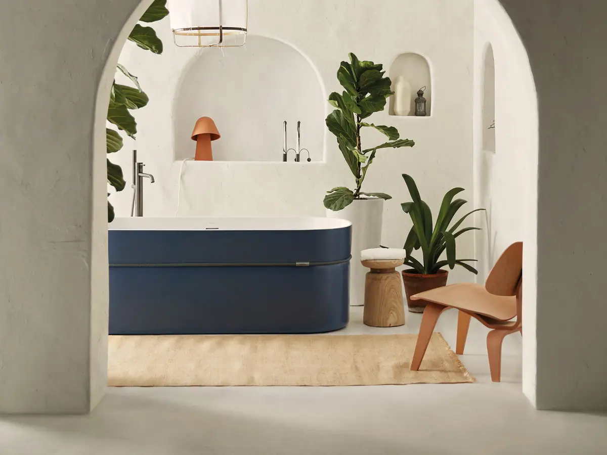 Bañera exenta Tempo con el exterior azul y una cuerda alrededor, en un baño blanco con arcos y plantas