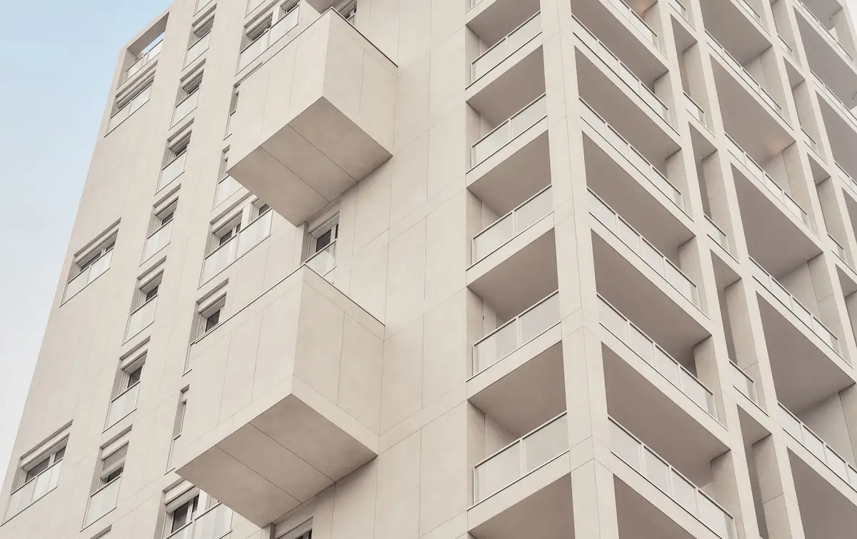 Fachada de un edificio de viviendas revestida con grandes placas cerámicas de color crema, con balcones y volúmenes en voladizo.
