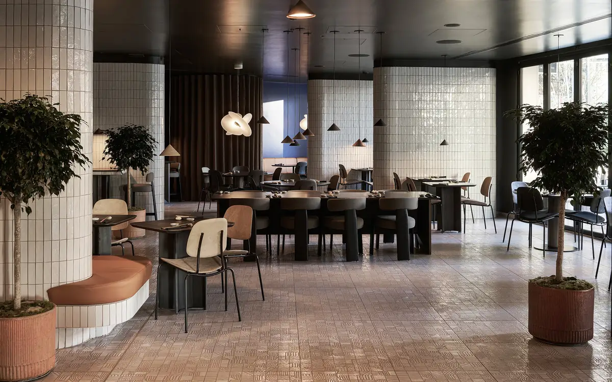 Comedor de restaurante con columnas revestidas de azulejo blanco y suelo cerámico con dibujo geométrico en tonos tierra.