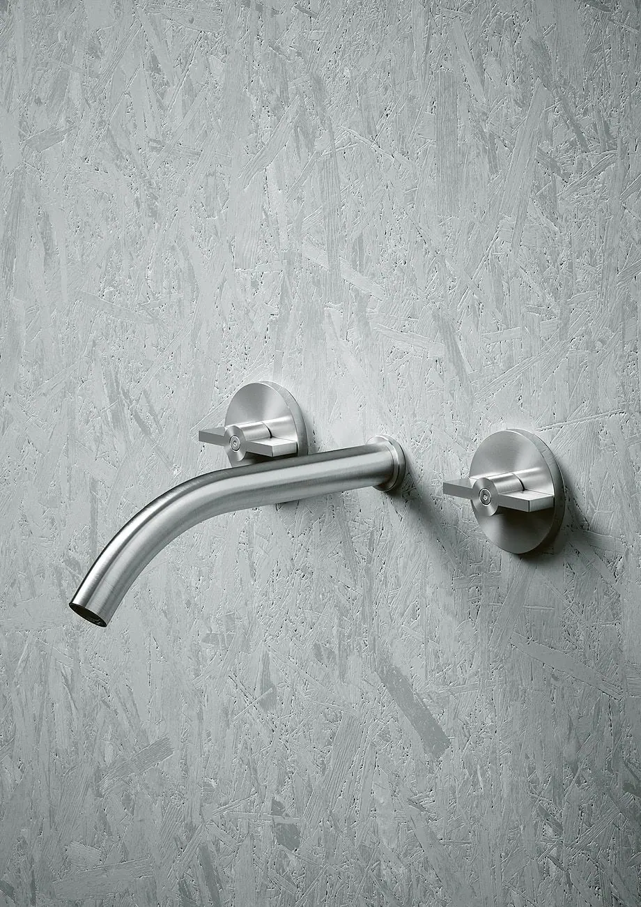Curved steel wall spout between two round handles on a textured grey wall