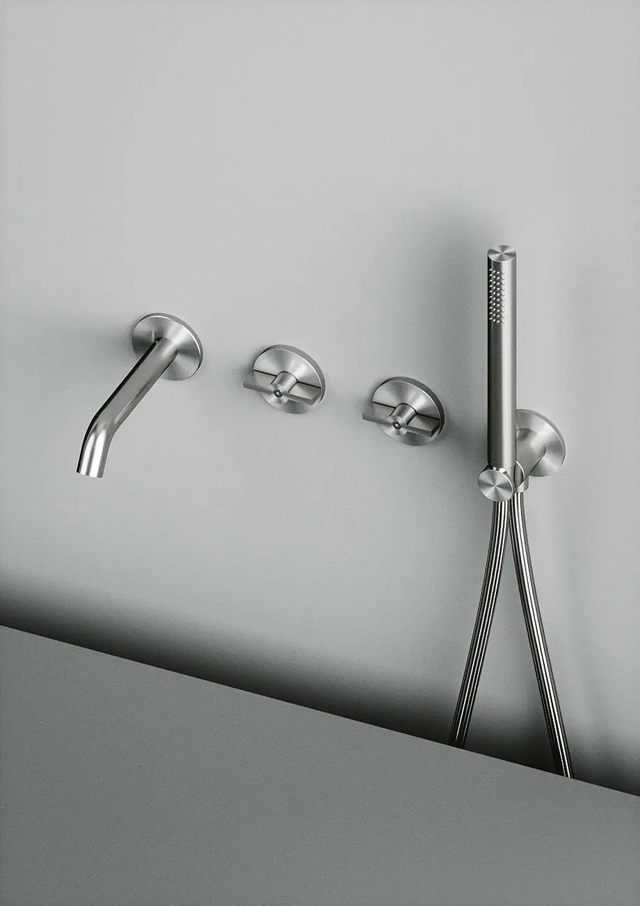 Wall spout, two round handles and hand shower with steel holder on a grey wall