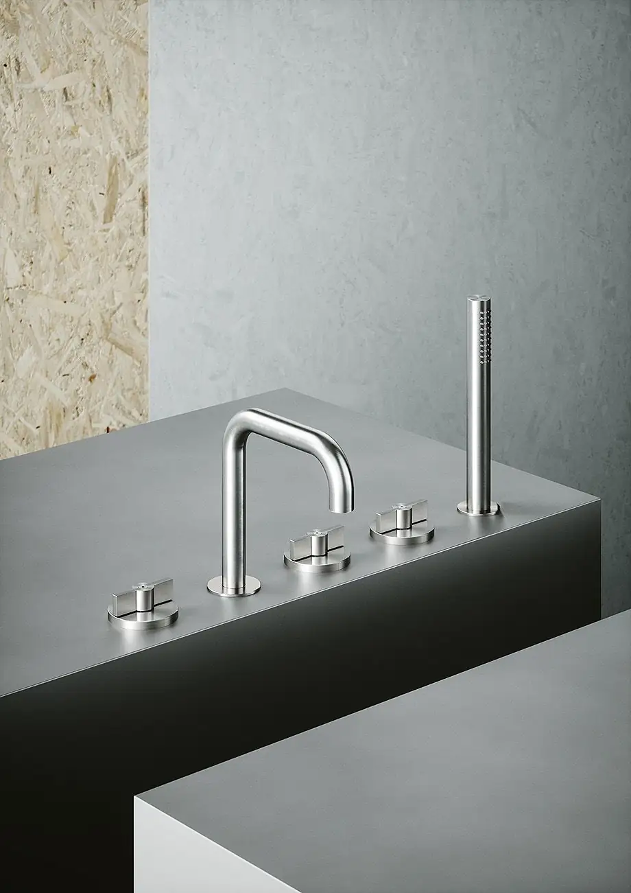 Steel bath-rim tap with spout, three handles and hand shower on a grey surface
