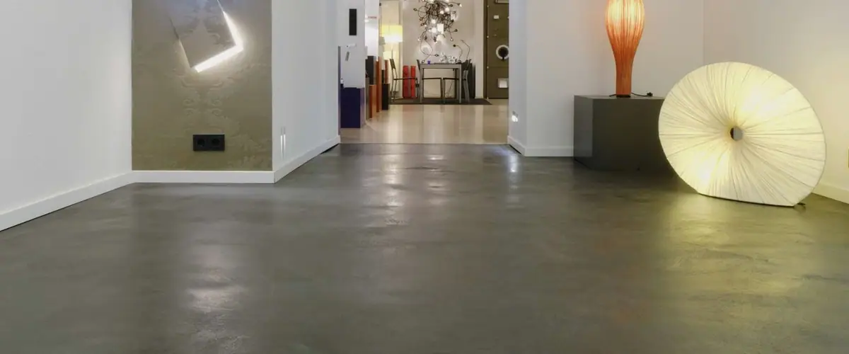 Pavimento continuo de base cementosa gris oscuro con reflejos en un espacio comercial con lámparas de diseño