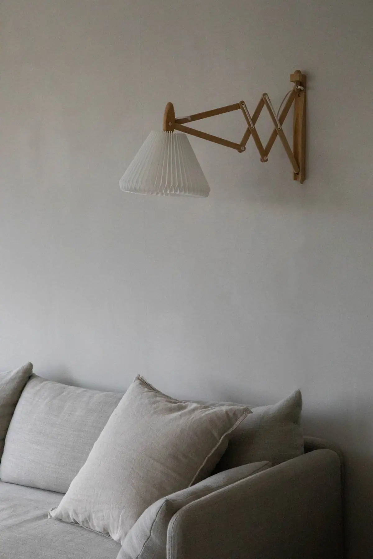 Aplique de brazo extensible con pantalla plisada sobre un sofá de lino, ante una pared de yeso claro