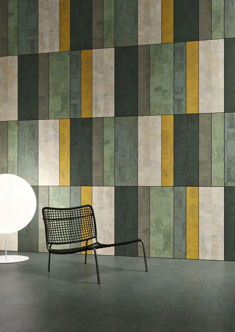 Wall of vertical cork pieces in greens, whites and yellow, with a black cane chair and a globe lamp