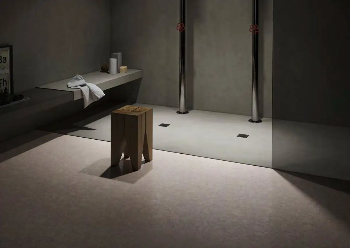 Dimly lit bathroom with a walk-in shower, a built-in bench, a wooden stool and a pale speckled floor