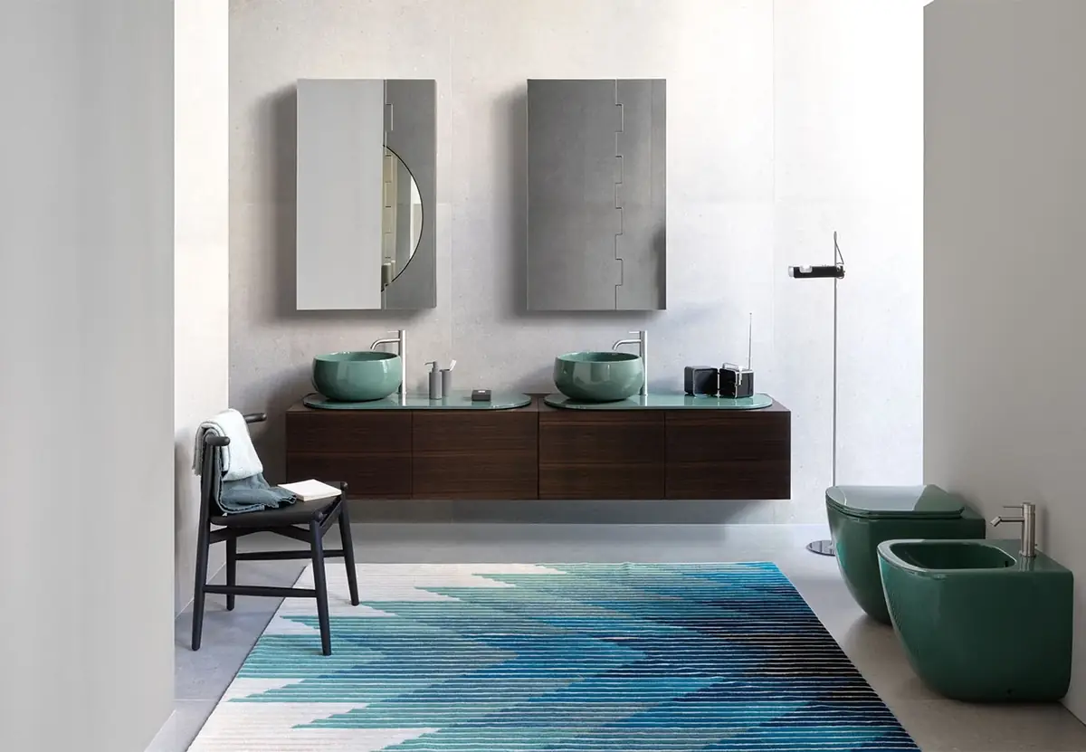 Dos lavabos de apoyo verde brillante sobre tops ovalados del mismo color y un mueble suspendido de madera oscura, con inodoro y bidé verdes