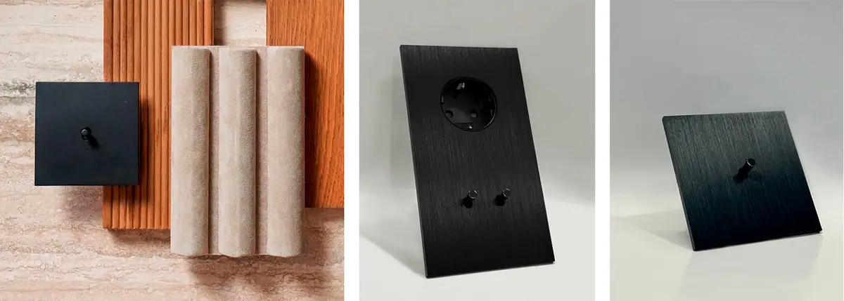 Interruptores Atelier en negro: placa cuadrada sobre muestras de madera y piedra, panel con enchufe y dos palancas, y placa con una palanca.