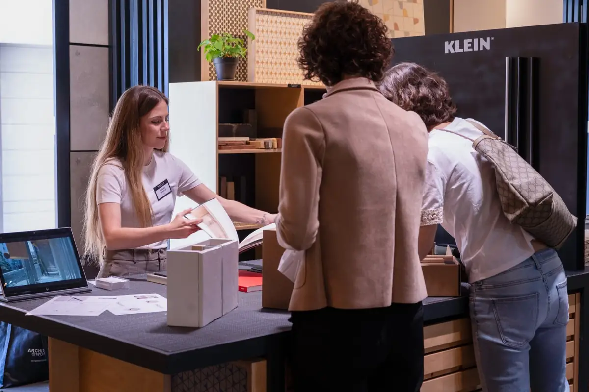 Una representante atiende a dos visitantes junto al expositor de Klein