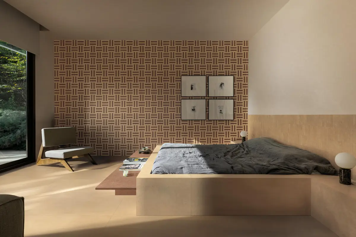 Dormitorio con pared revestida de un trenzado de piezas rosadas y rojizas y suelo de porcelánico arena