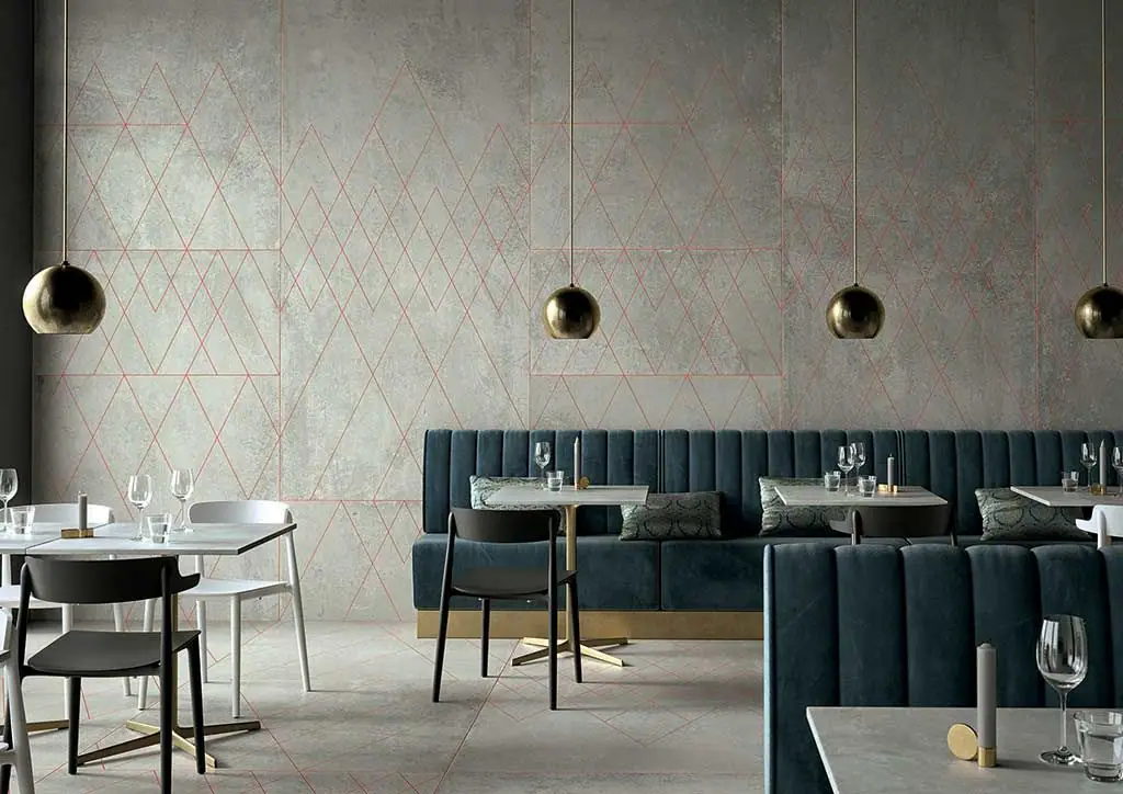 Restaurant with a blue upholstered banquette and a wall in grey cement-effect porcelain with a geometric line decoration