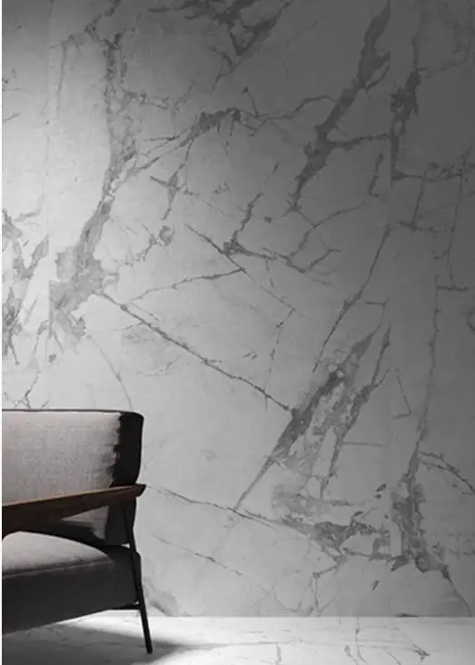 Wall clad in white marble-effect porcelain with grey veining and a dark armchair in front