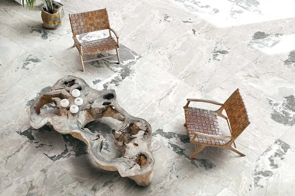 Large-format porcelain floor with a light stone effect and dark patches, with two leather armchairs and a tree-trunk table