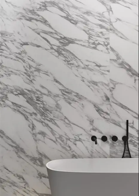 Bathroom wall clad in white marble-effect porcelain with grey veining, with black taps and a white bath