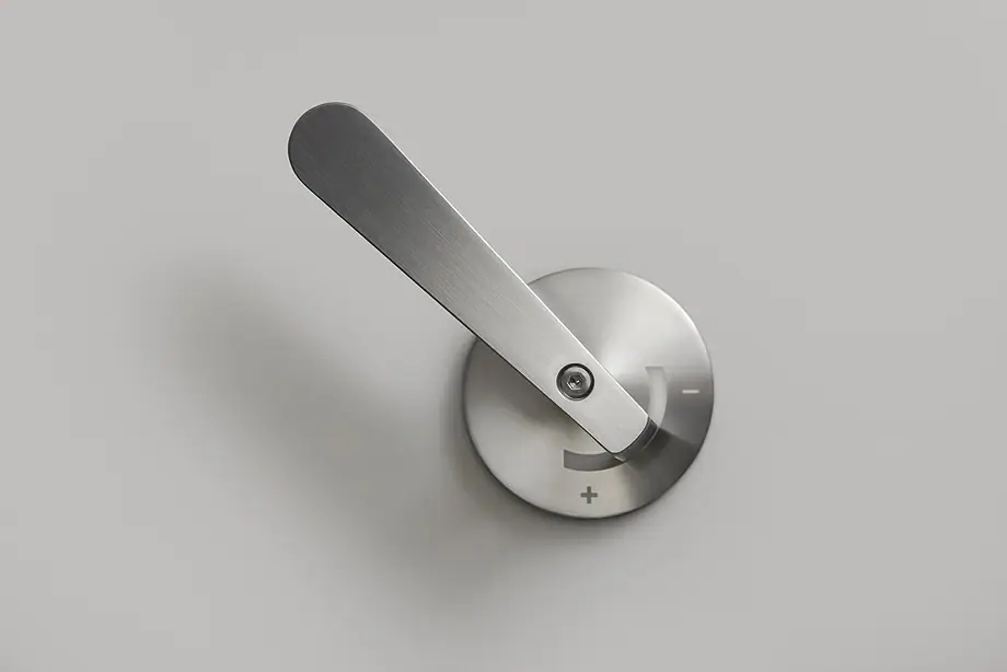 Elongated satin steel handle mounted on the wall on a round escutcheon with plus and minus markings