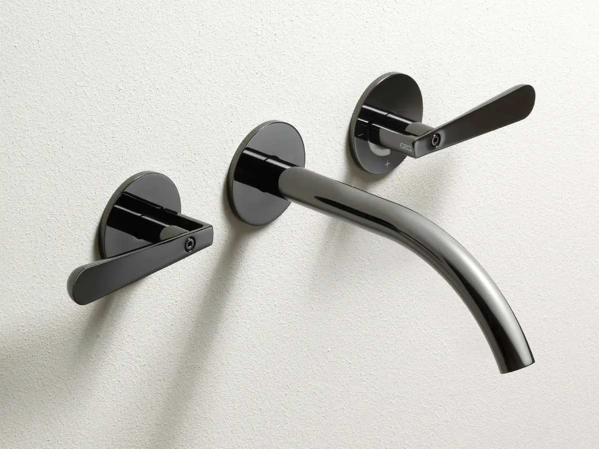 Wall-mounted basin tap with two handles and a curved spout in a glossy black finish on a white wall