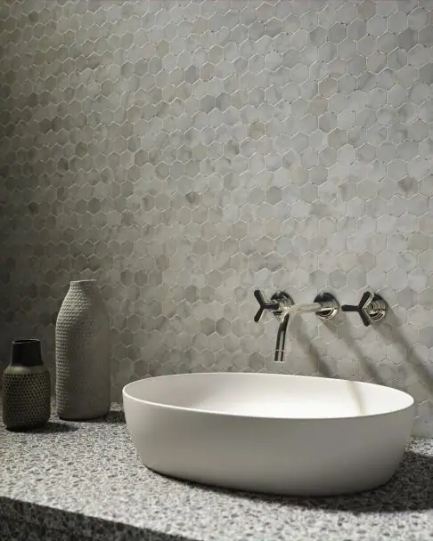 Batería de lavabo empotrada con dos mandos de cruceta de tres radios y caño curvo, sobre una pared de mosaico hexagonal de mármol