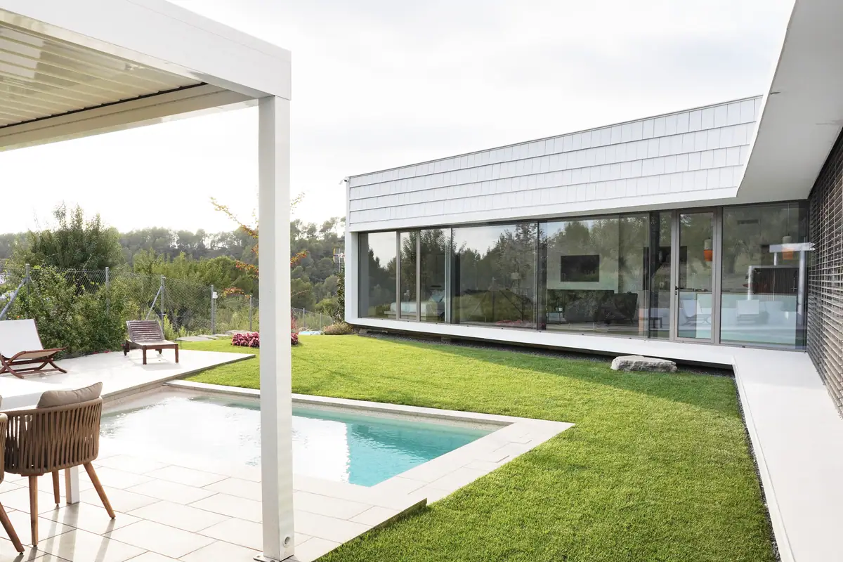 Garden and swimming pool of Casa Om, with the glazed façade of the house and white slatted cladding on the upper part