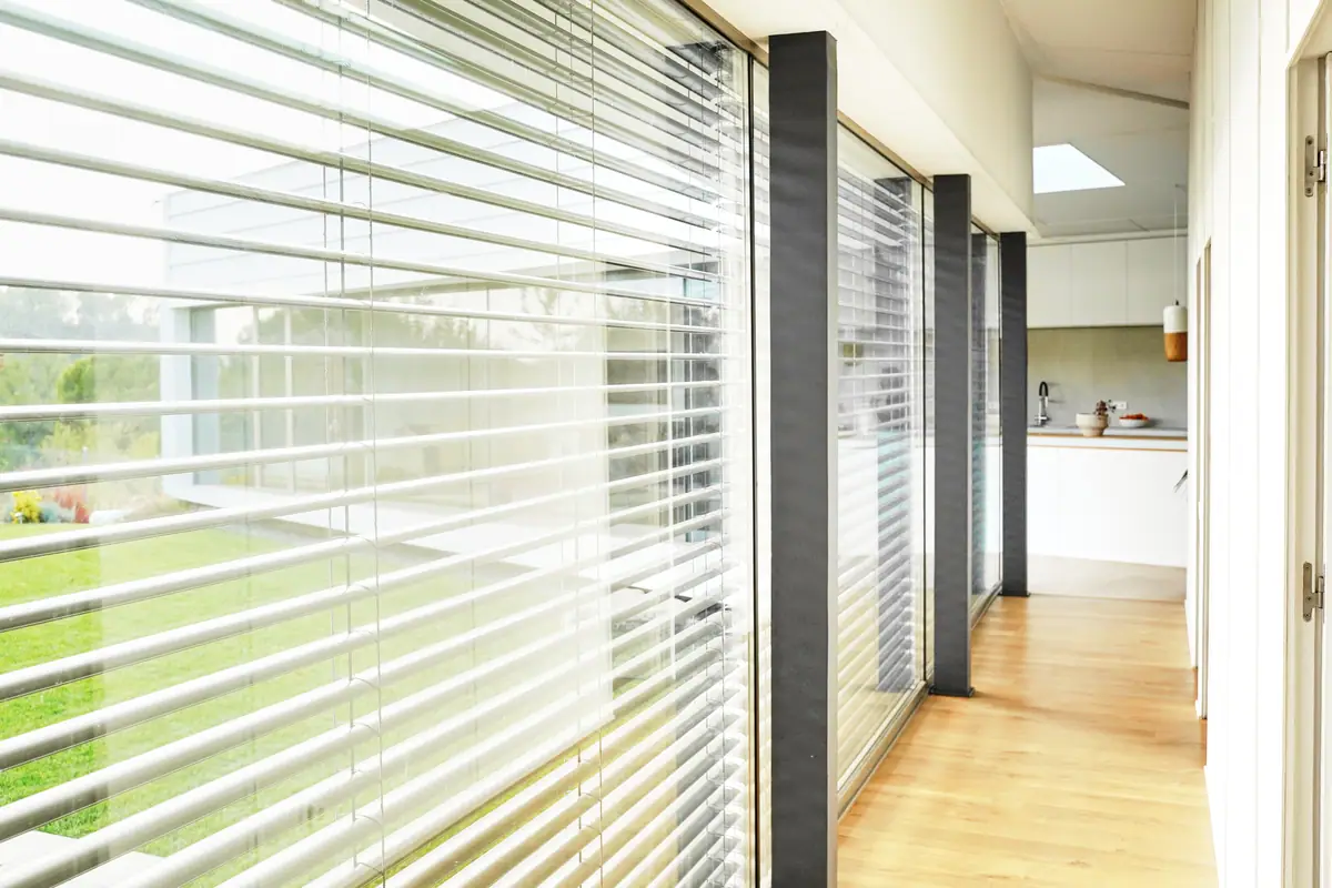 Interior gallery of Casa Om next to the glazed façade, with slatted venetian blinds and a wooden floor