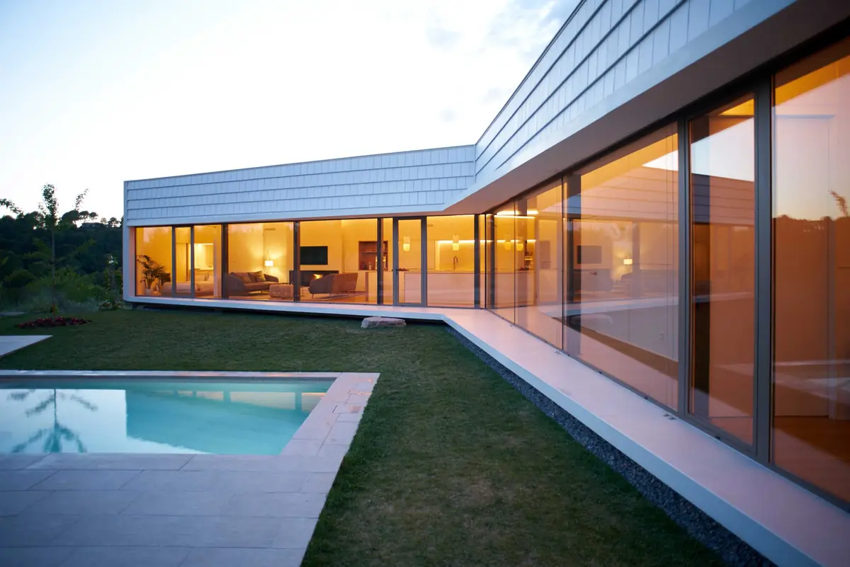 Casa Om at dusk, with the illuminated glazing surrounding the garden and the swimming pool