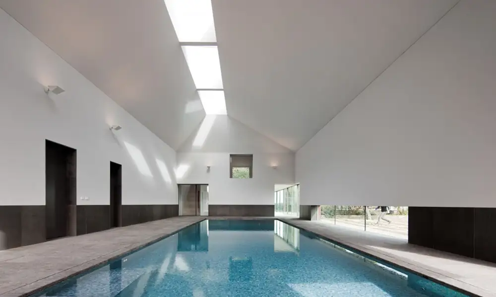 Indoor pool with a sloping white ceiling, longitudinal rooflight and dark plinth.