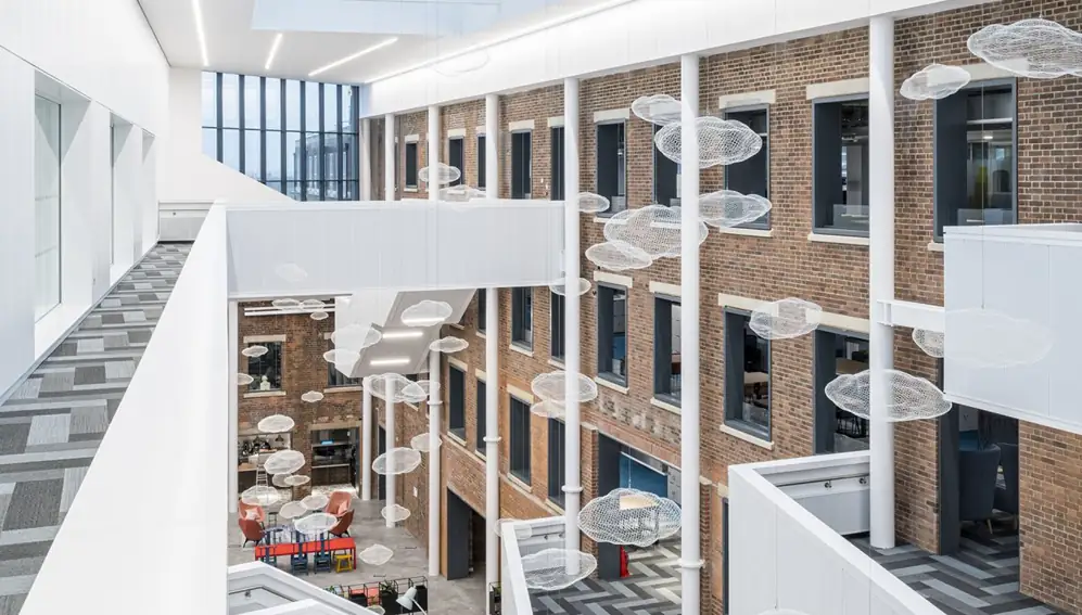 Multi-storey atrium with white balustrades, exposed brick walls and suspended cloud-shaped sculptures.