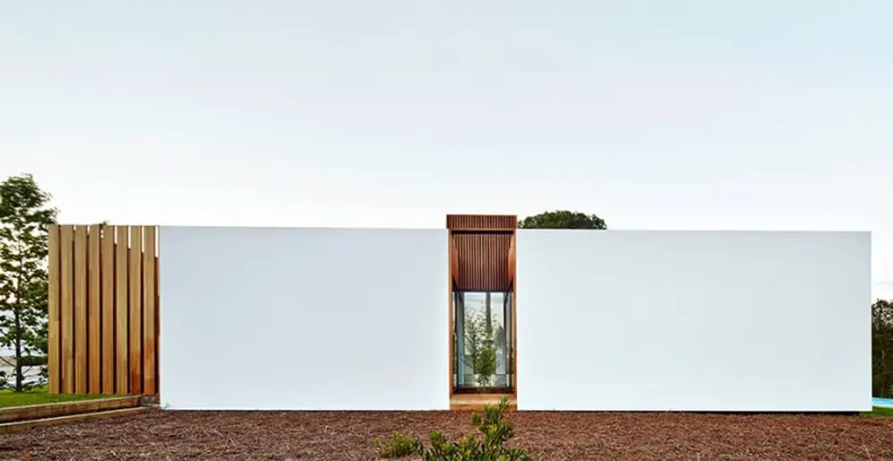 Single-storey house with a continuous white façade, a tall timber entrance and a timber slatted screen.