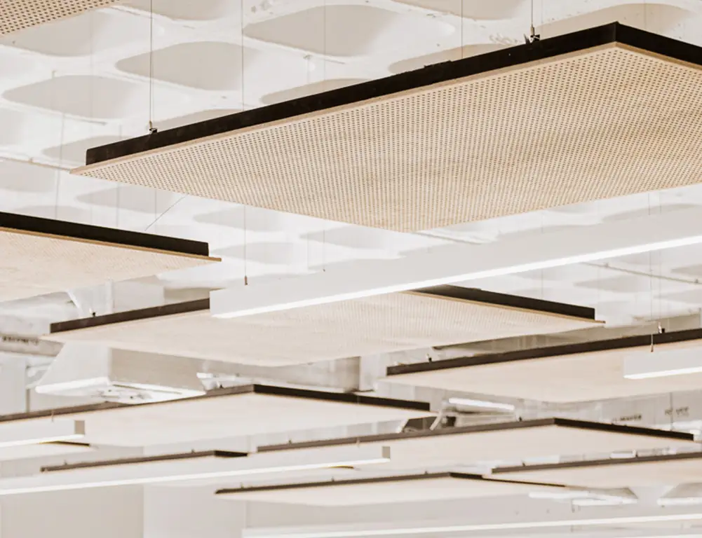 Suspended acoustic islands of perforated board with black frames beneath a white waffle slab.