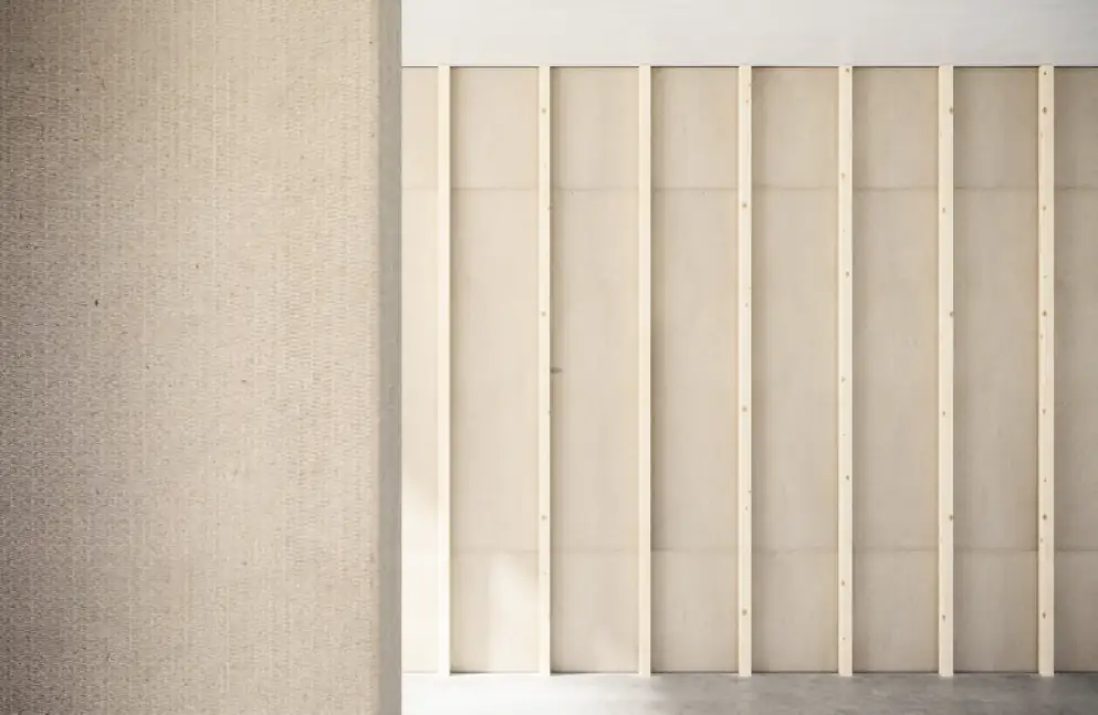 Wall clad with a finely textured beige board next to a partition of pale boards on timber battens.
