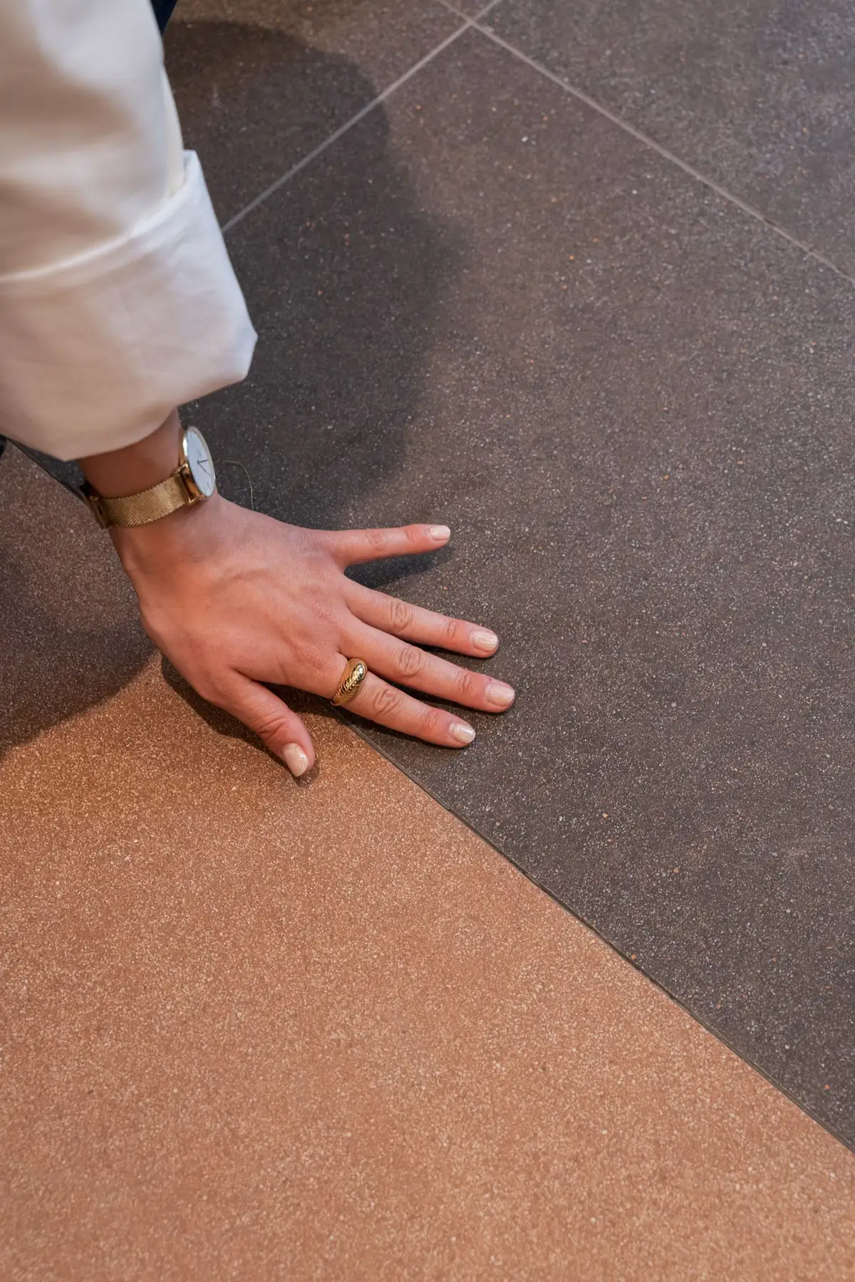 A hand resting on a fine-grained ceramic floor in two tones, brown and terracotta